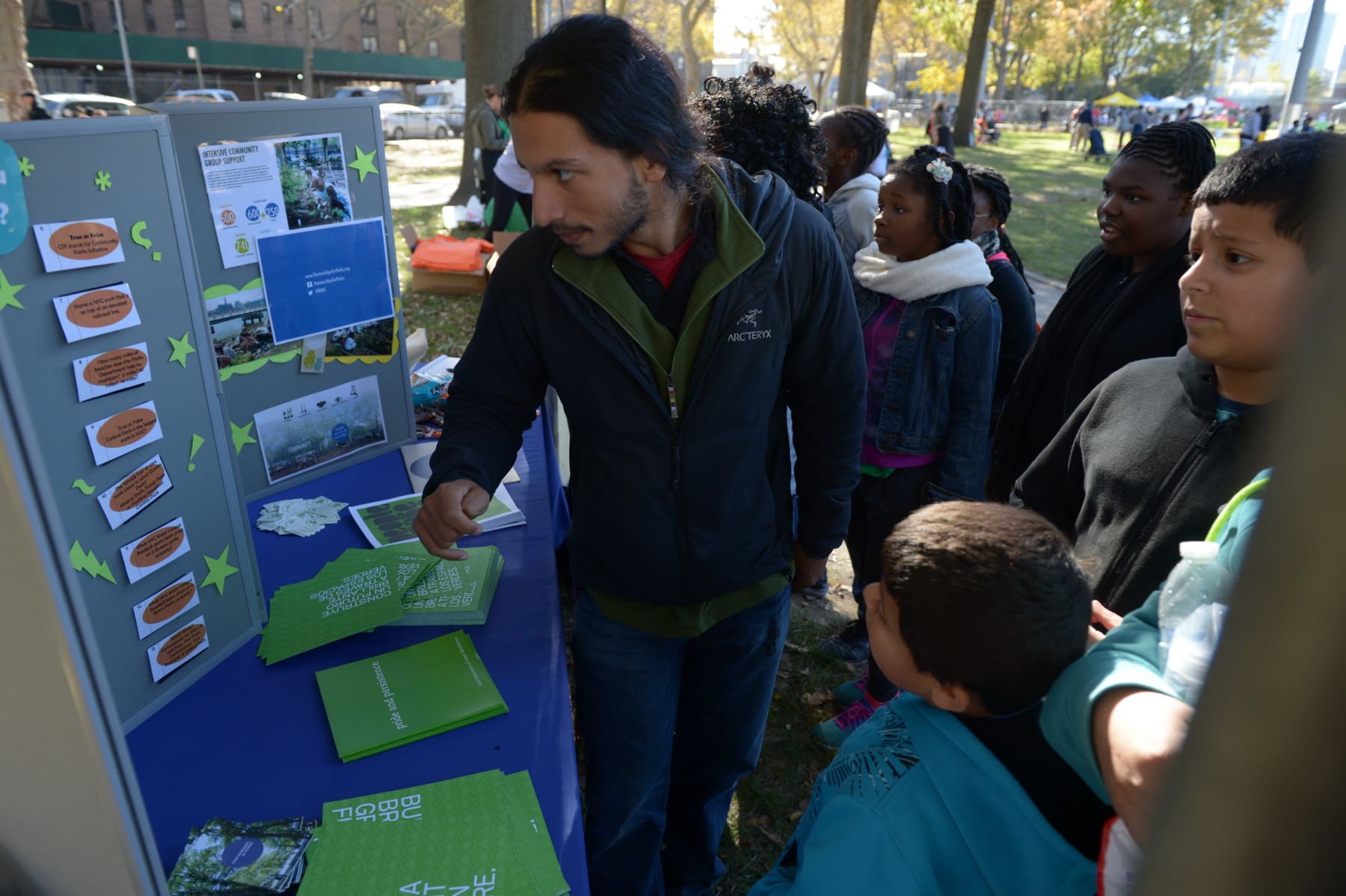 Community members engage with a Partnerships for Parks staff member at a community information booth. They are under a roofed-area in a New York City park.