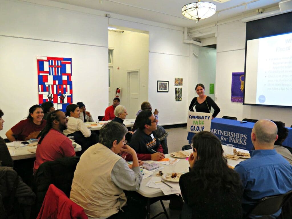 A diverse group of participants sit together at different tables listening to a Partnerships for Parks staff member conduct a workshop.