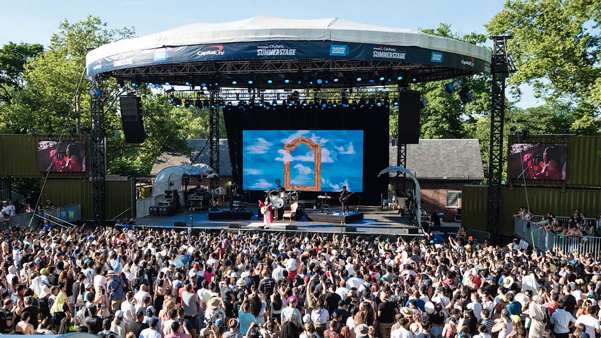 A day-time shot of the stage at SummerStage in Central Park. A large diverse crowd is watching Latin Alternative artist Carla Morrison on stage.