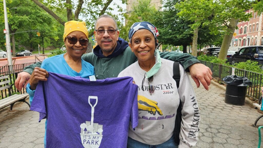 a group of people posing for a picture outdoors with a purple shirt in foreground with a shovel graphic on it.