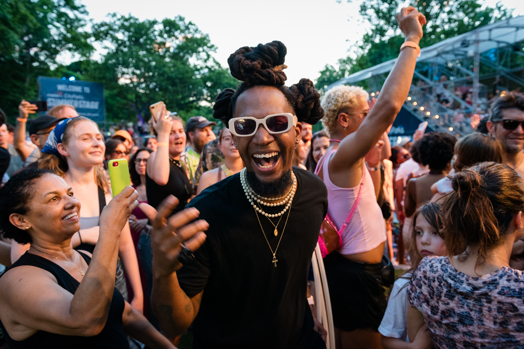 A black man with sunglasses on standing in front of a crowd of people at a live music show.