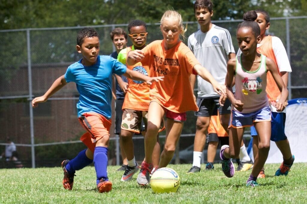 A group of young children are playing soccer on a grassy field. Two children are racing for the soccer in the front of the group.