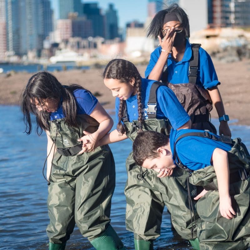 Four young children standing in a lake in waders staring at the water