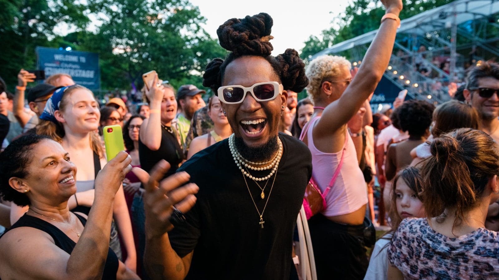 A black man with sunglasses on standing in front of a crowd of people at a live music show.