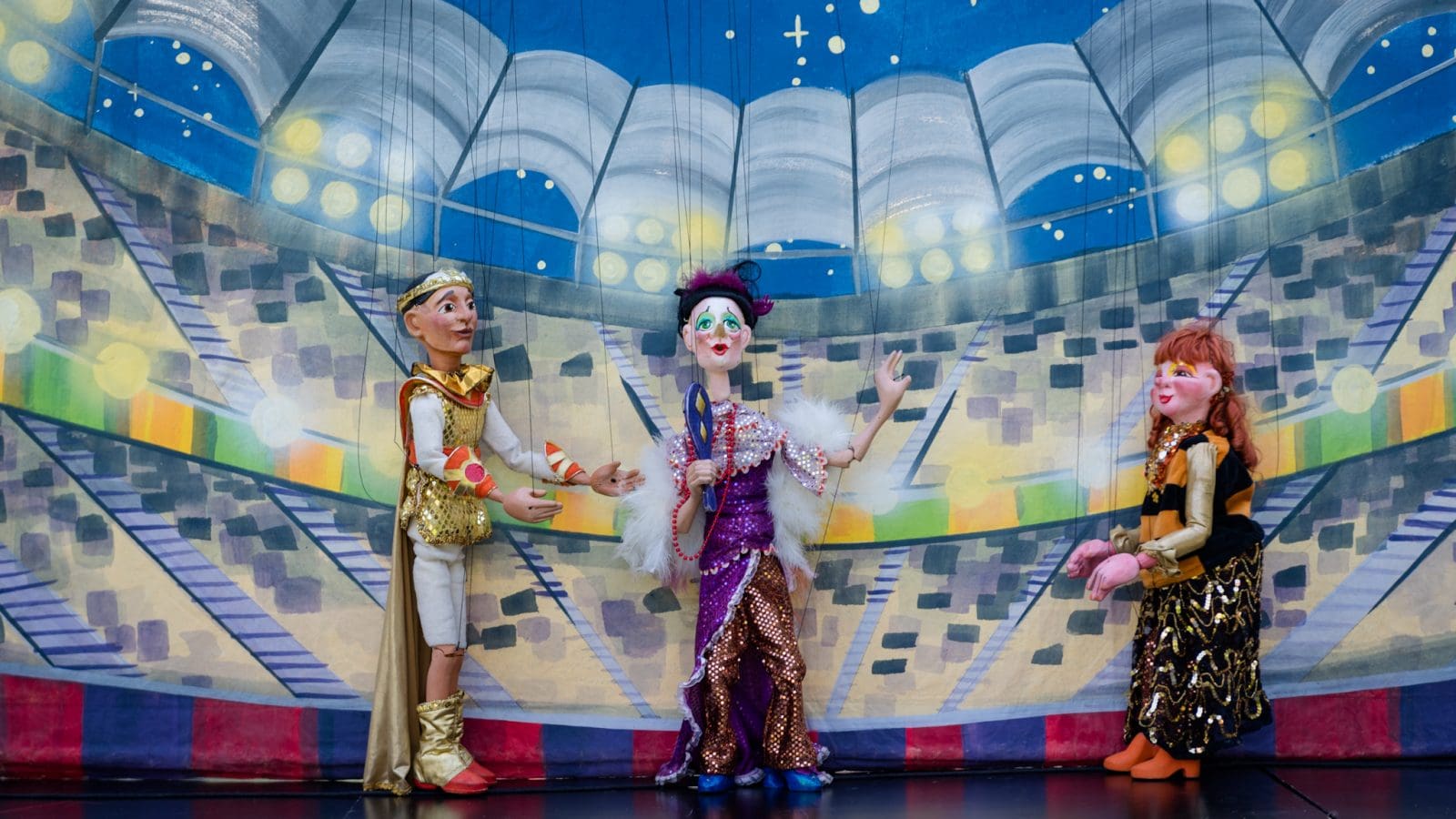 Three marionette puppets on a stage with a theater in the background.