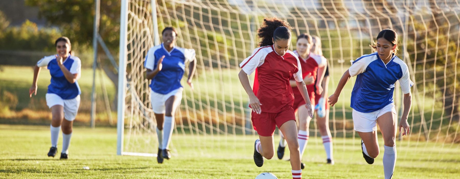 Sports team, girl soccer and kick ball on field in a tournament. Football, competition and athletic female teen group play game on grass. Fit adolescents compete to win match at school championship