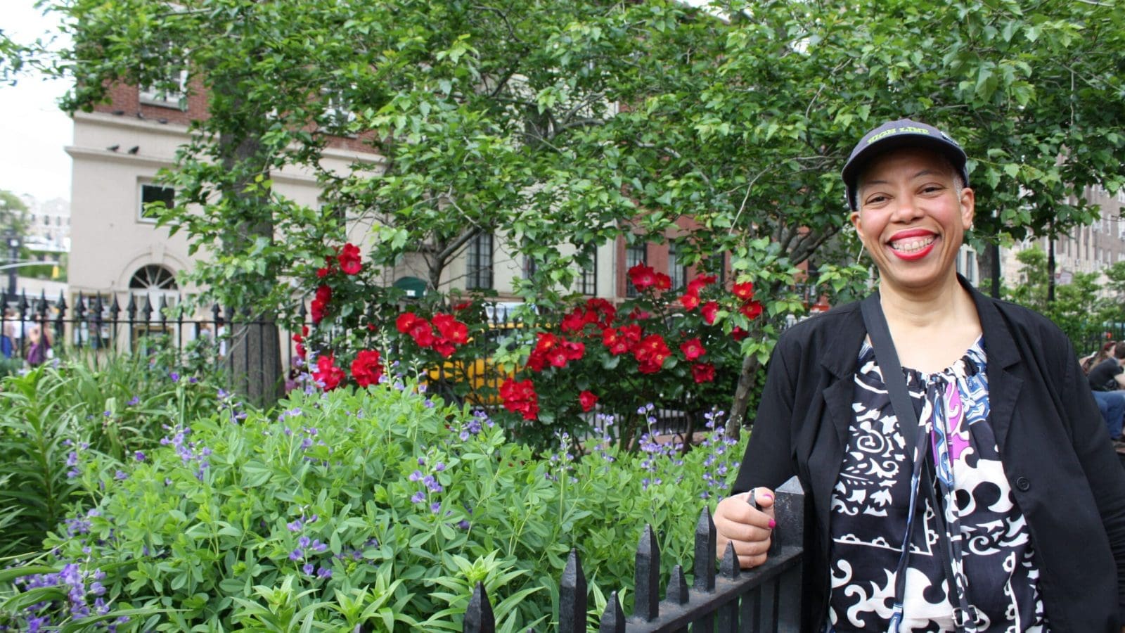 A smiling Black woman stands next to colorful flowers in a New York City park.