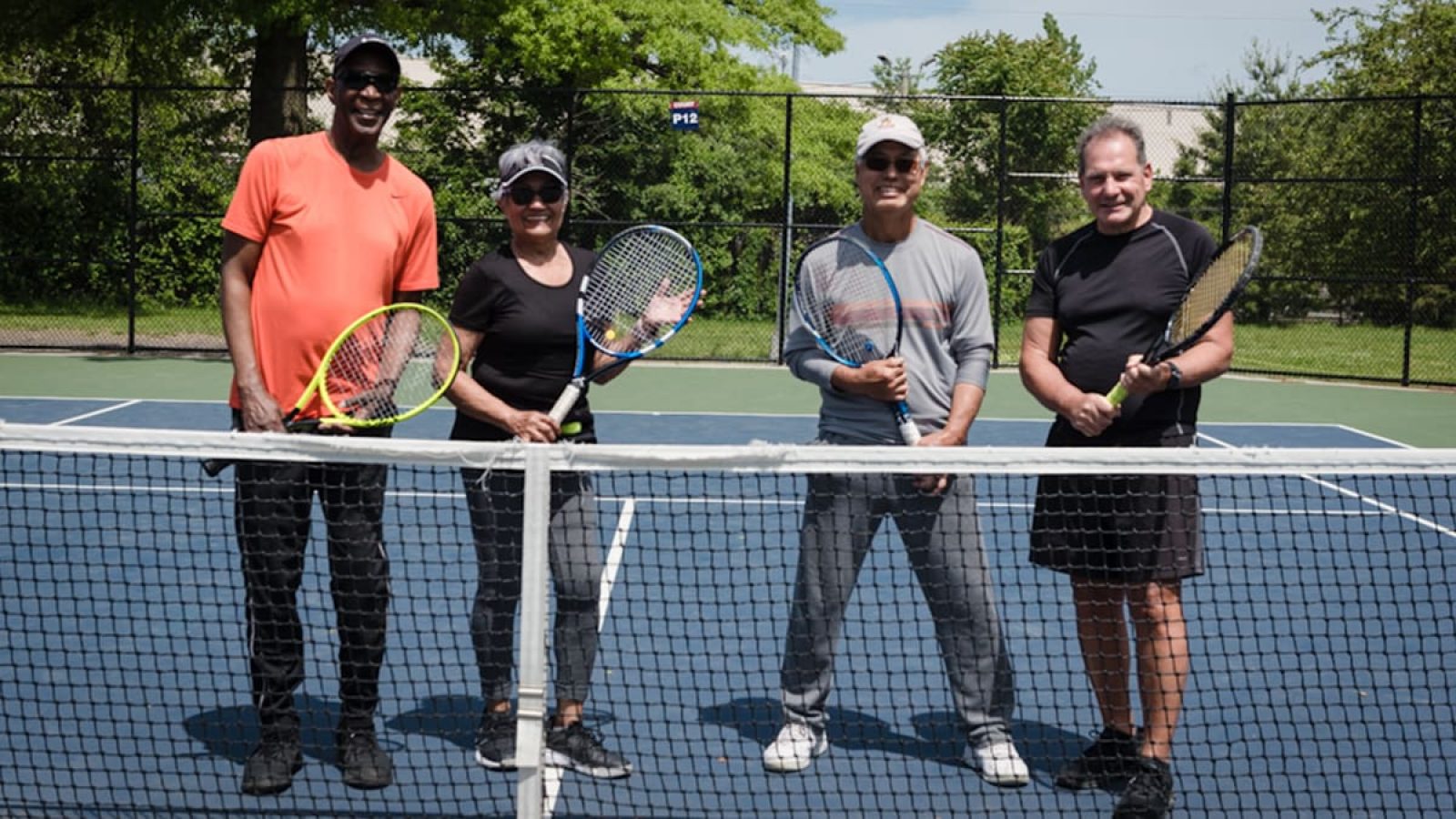A group of four adults are standing on a tennis court with tennis racquets in their hands.