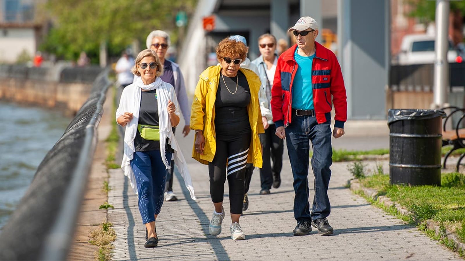 A large group of adults are walking on a sidewalk next to a body of water.