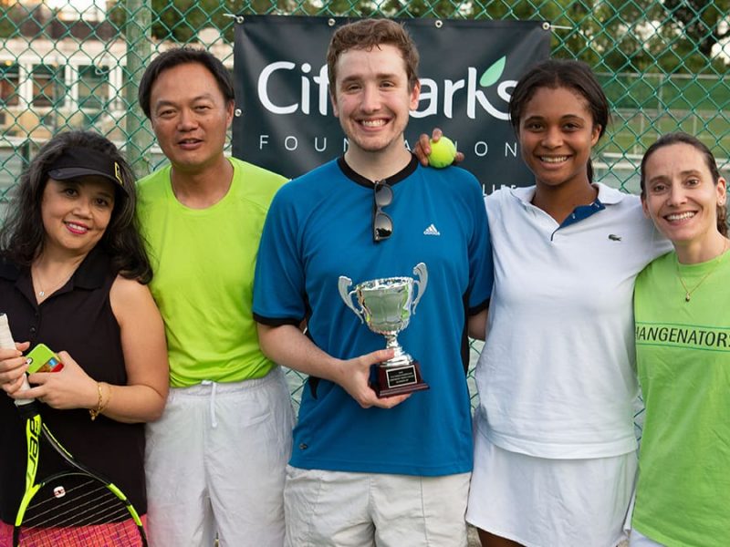 A smiling company team - of various ages, genders and races - participating in our corporate tennis league, smiling and holding a trophy after a tournament