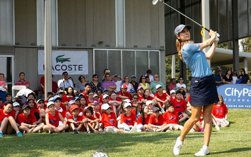 Thumbnail: A golf pro teaching a clinic to City Parks Foundation golf students, with sponsor Lacoste in the background.