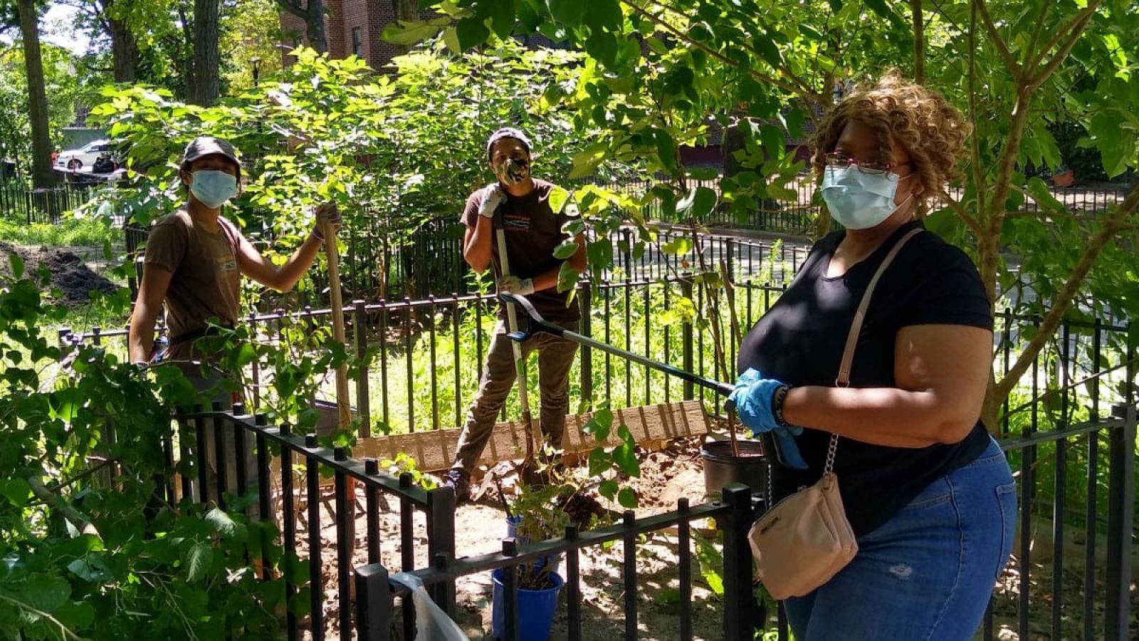 Three masked volunteers stand together with tools in their hands in a New York City park.