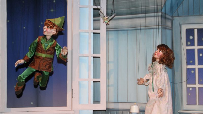 A photo from a performance of Neverland at the Swedish Cottage Marionette Theatre. It features a Peter Pan puppet flying through Wendy's window.