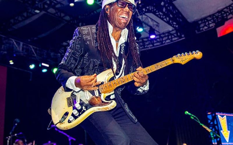 A thumbnail photo of artist Nile Rodgers performing on-stage.