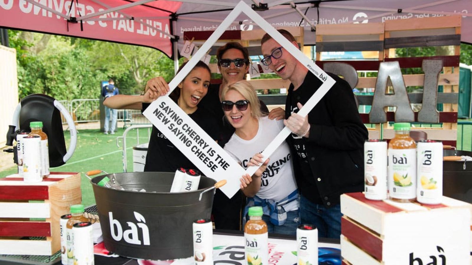 A group of people smiling for a sponsor at SummerStage. There in their booth with various products and giveways out.