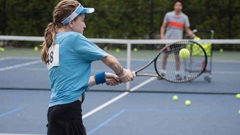 Young tennis player in blue shirt hitting ball